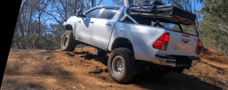 Pick-up Toyota bianco carico di attrezzatura da campeggio posizionato su terreno roccioso nella boscaglia australiana che dimostra condizioni fuoristrada con carico pesante