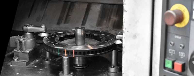 Processo di produzione ad alta precisione DBA che mostra un disco freno con indicatori in vernice termica durante la produzione Disco freno DBA con indicatori di temperatura colorati in fase di lavorazione su macchina CNC di precisione con pannello di controllo visibile sullo sfondo