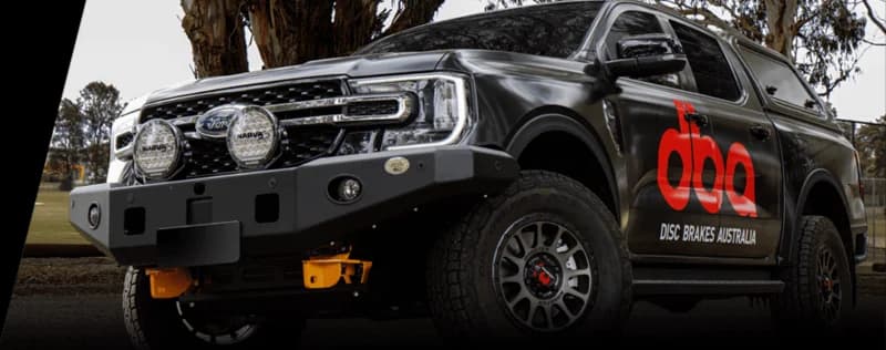 DBA sul campo Pick-up scuro a marchio DBA Disc Brakes Australia con logo DBA rosso e attrezzature di illuminazione aggiuntive in ambiente esterno