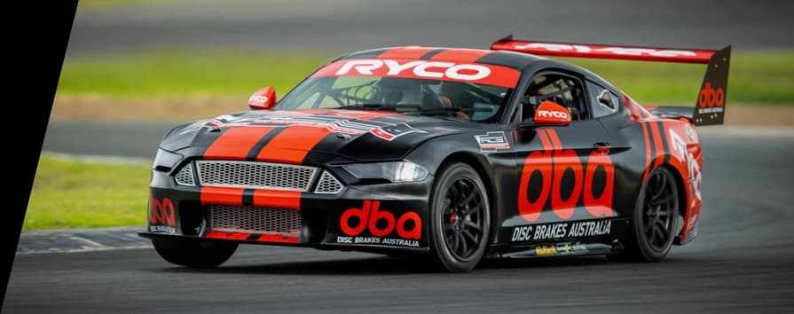 Veicolo motorsport professionale equipaggiato con impianti frenanti ad alte prestazioni DBA in condizioni di gara Auto da corsa sponsorizzata DBA in pista con livrea rossa e nera e marchio DBA durante una gara su circuito