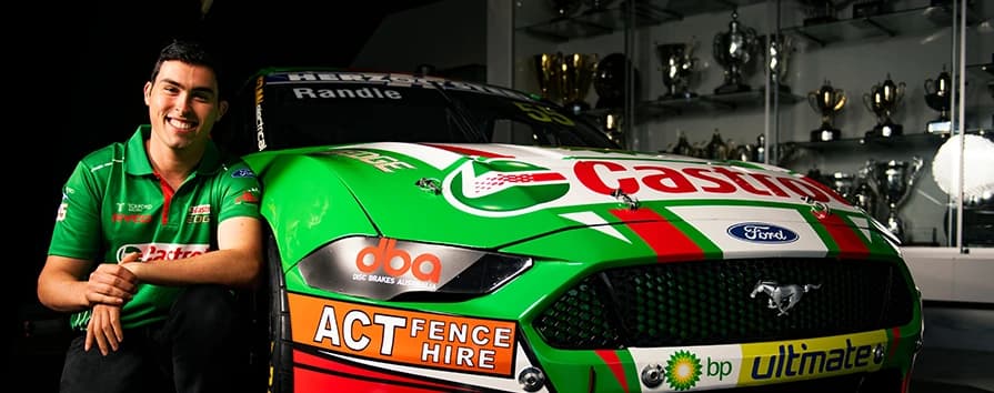 Pilota motorsport professionale con veicolo del Supercars Championship sponsorizzato da DBA che mostra la partnership di gara e la tecnologia di frenata ad alte prestazioni Pilota di auto da corsa sorridente in maglia verde della squadra in piedi accanto all'auto da corsa Ford Mustang verde sponsorizzata da DBA con molteplici loghi di sponsor esposti nella sala trofei