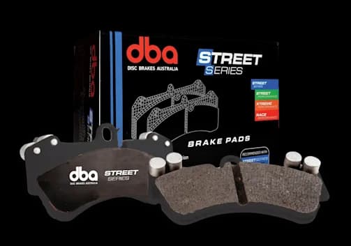 Pastiglie freno DBA Street Series per ricambio OE e applicazioni di guida quotidiana Pastiglie freno DBA Street Series caratterizzate da piattelli metallici neri con materiale d'attrito mostrate accanto alla confezione di vendita