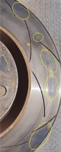 Disco freno con depositi di materiale d'attrito visibili che possono portare a vibrazioni del volante e prestazioni di frenata irregolari Primo piano della superficie del disco freno che mostra depositi irregolari di materiale d'attrito evidenziati con cerchi gialli che causano la vibrazione in frenata