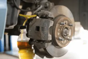 Liquido freni e bolle d'aria che vengono espulsi attraverso la valvola di spurgo nel contenitore di raccolta durante la corretta sequenza di spurgo dei freni Pinza freno con tubo di raccolta giallo collegato alla valvola di spurgo che mostra il liquido freni di colore ambra che fluisce nel contenitore trasparente durante lo spurgo