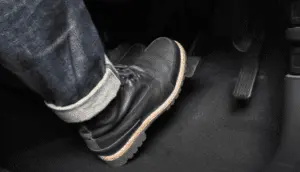 L'assistente applica una pressione decisa sul pedale del freno durante il processo di spurgo per spingere il liquido e l'aria attraverso i tubi freno Primo piano del piede di una persona che preme con decisione il pedale del freno durante la procedura di spurgo per creare pressione idraulica nel sistema