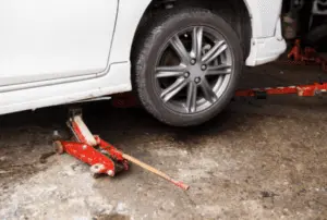 Configurazione con cric idraulico da carrello e cavalletti di sicurezza per sollevare in sicurezza il veicolo durante la procedura di spurgo dell'impianto frenante Cric idraulico da carrello posizionato sotto il veicolo con cavalletti di sicurezza visibili per un supporto adeguato durante la manutenzione di spurgo dei freni