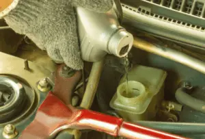 Rabbocco del liquido freni nel serbatoio della pompa freno per prevenire l'introduzione di aria durante il processo di spurgo dell'impianto frenante Mano con guanto del meccanico che versa liquido freni fresco nel serbatoio della pompa freno durante la procedura di spurgo per mantenere il livello di liquido corretto