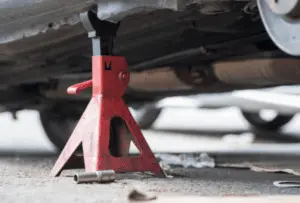 Cavalletto di sicurezza posizionato correttamente richiesto per il sollevamento sicuro del veicolo durante la procedura di spurgo dei freni Cavalletto di sicurezza rosso che sostiene il sottococca del veicolo nel punto di sollevamento designato per un accesso sicuro durante la manutenzione dei freni