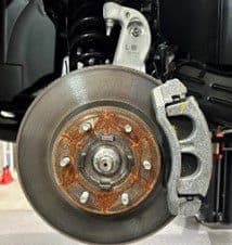 Passo 1A: Impianto frenante di primo equipaggiamento che mostra il disco e la pinza che verranno sostituiti durante la procedura di upgrade dei freni DBA Primo piano dell'impianto frenante di primo equipaggiamento (OE) che mostra la superficie del disco arrugginita, la pinza e la staffa di montaggio prima dell'installazione del kit di potenziamento freni DBA